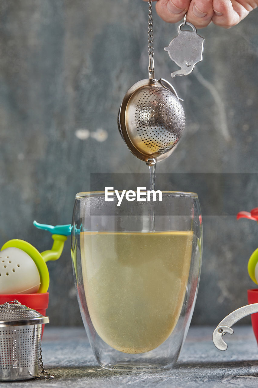 Brews tea in transparent glass with boiling water and tea strainer