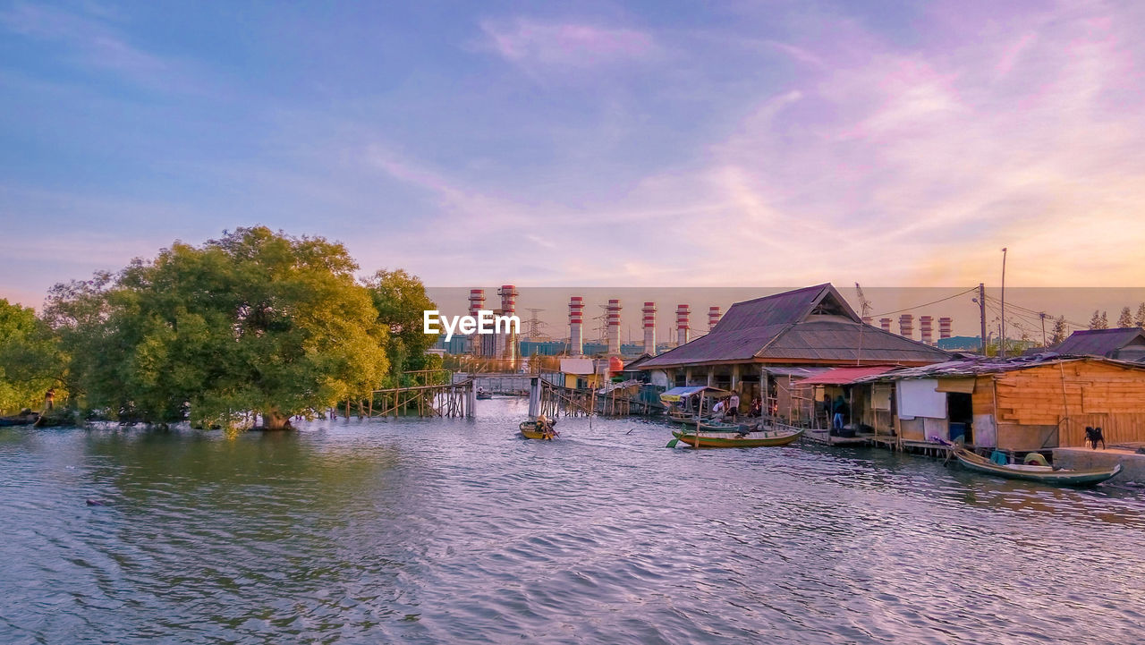 Scenic view of river by buildings against sky at sunset