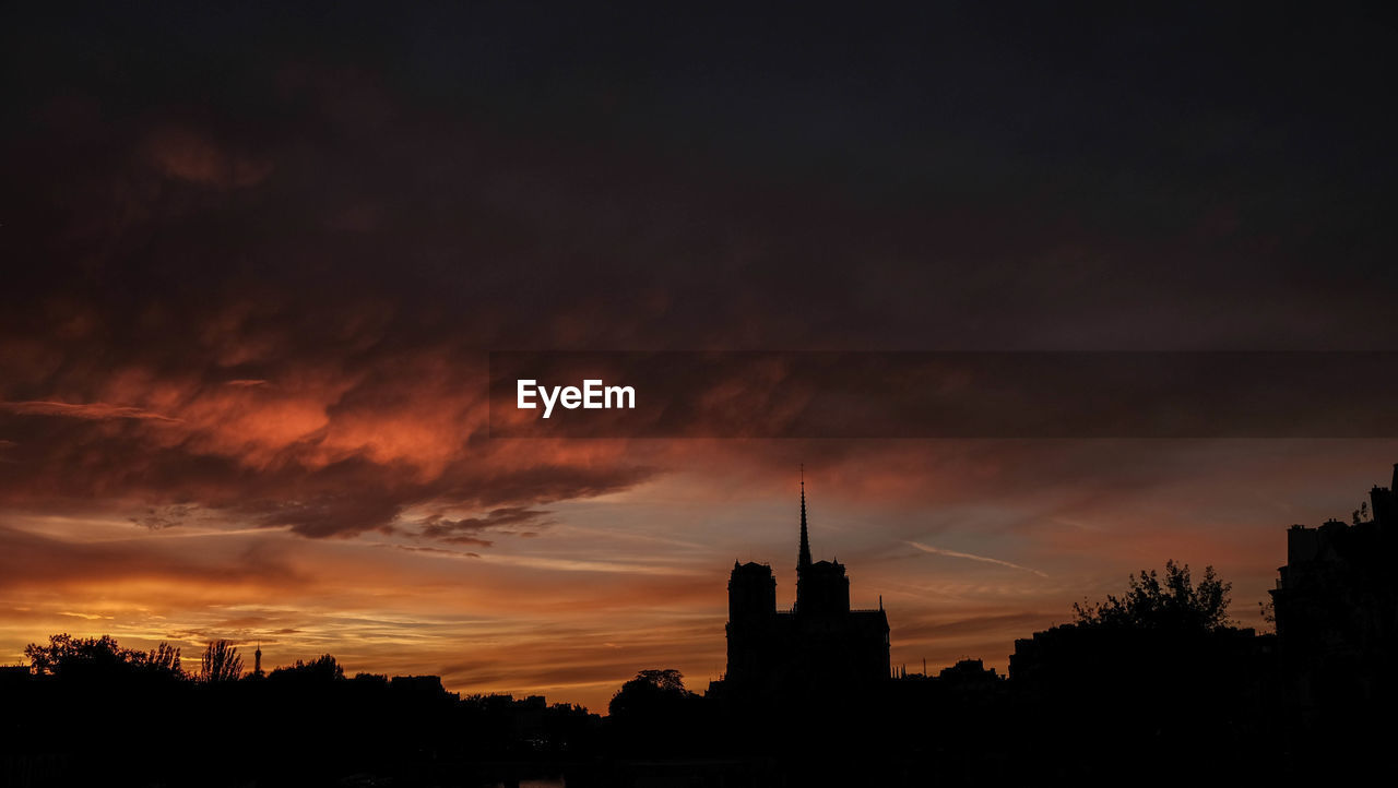 SILHOUETTE OF BUILDINGS AGAINST CLOUDY SKY