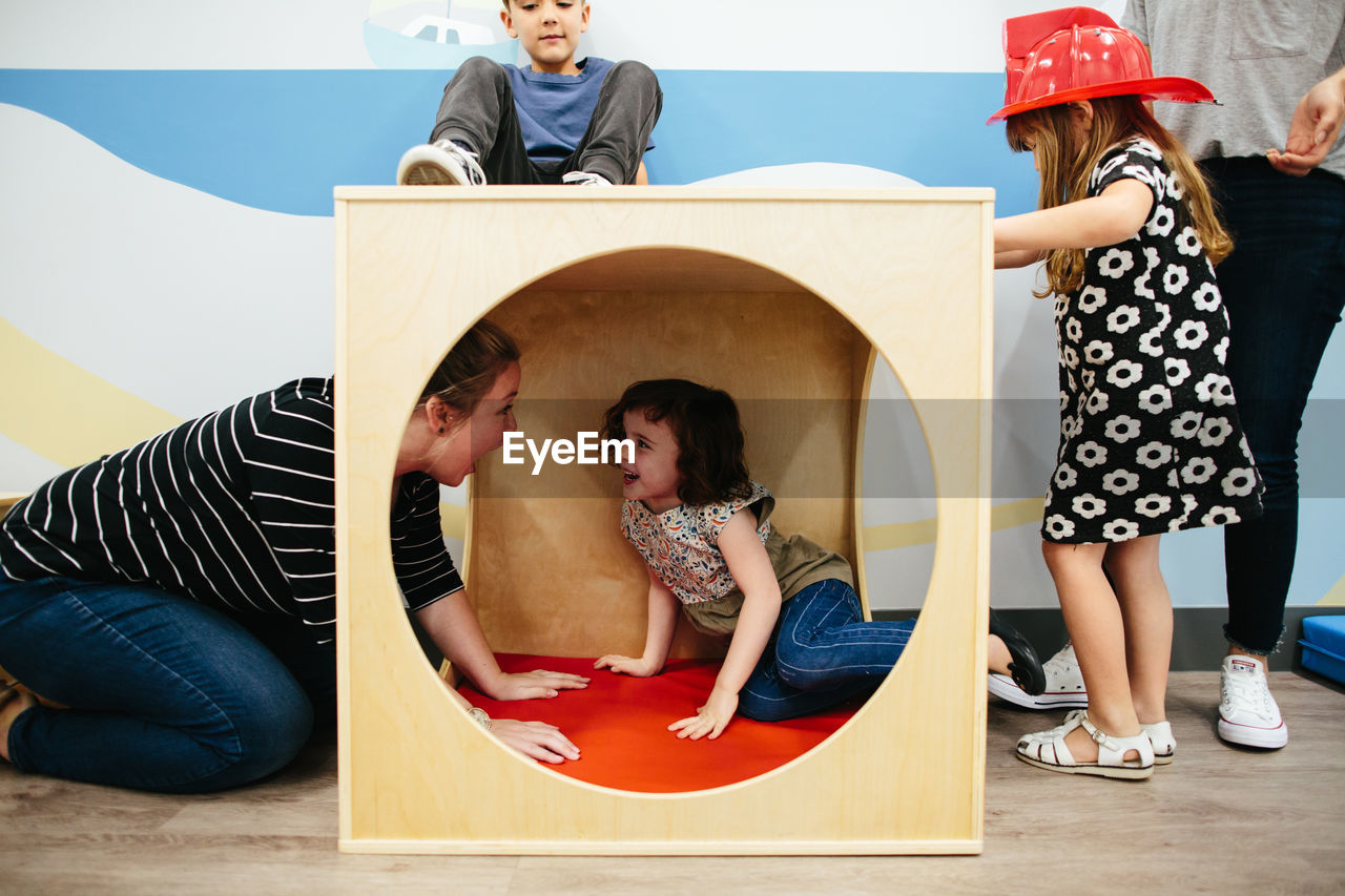 Girl inside a cube play structure smiles at her teacher