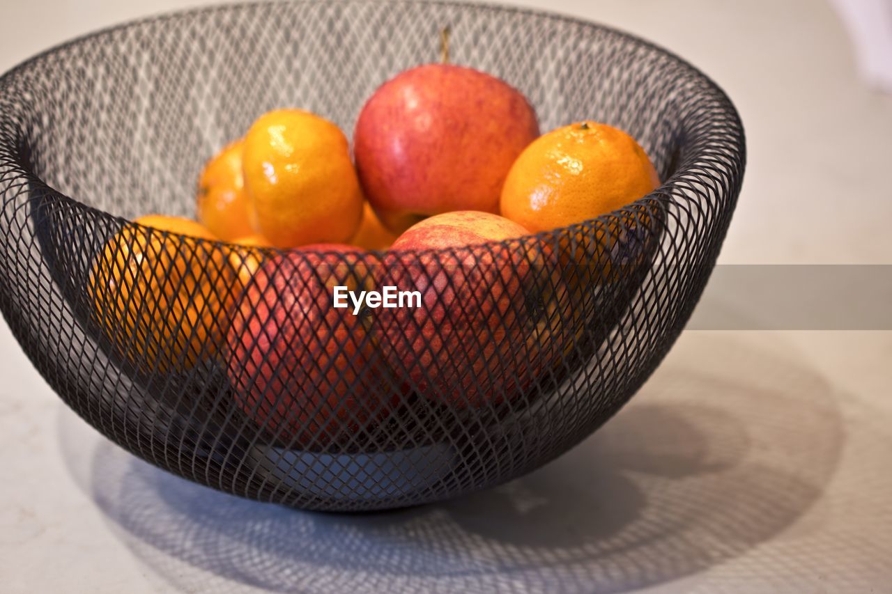 Apples and mandarins in a wire bowl inside on a kitchen bench