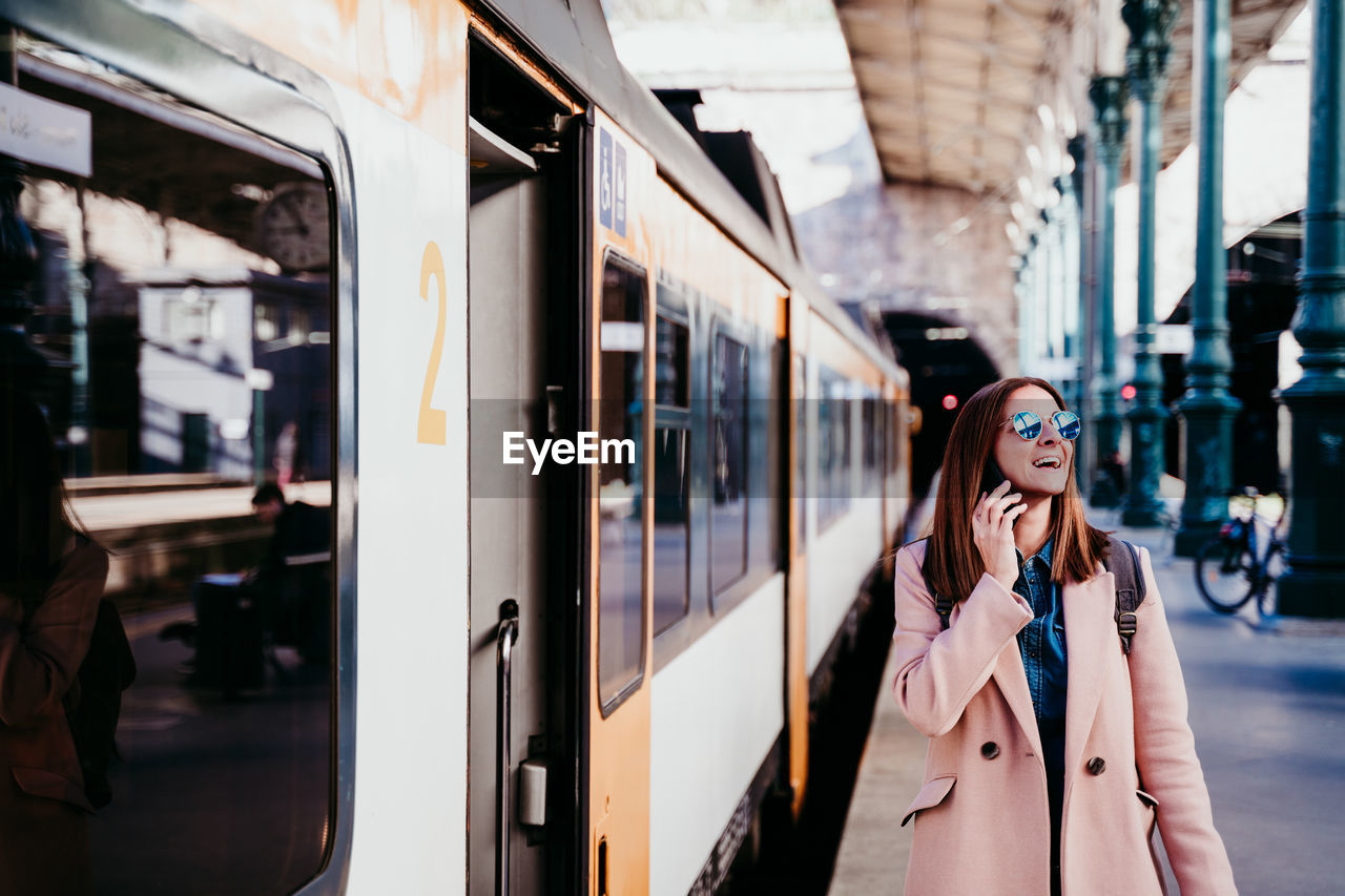 Woman with phone standing by train on railroad station platform