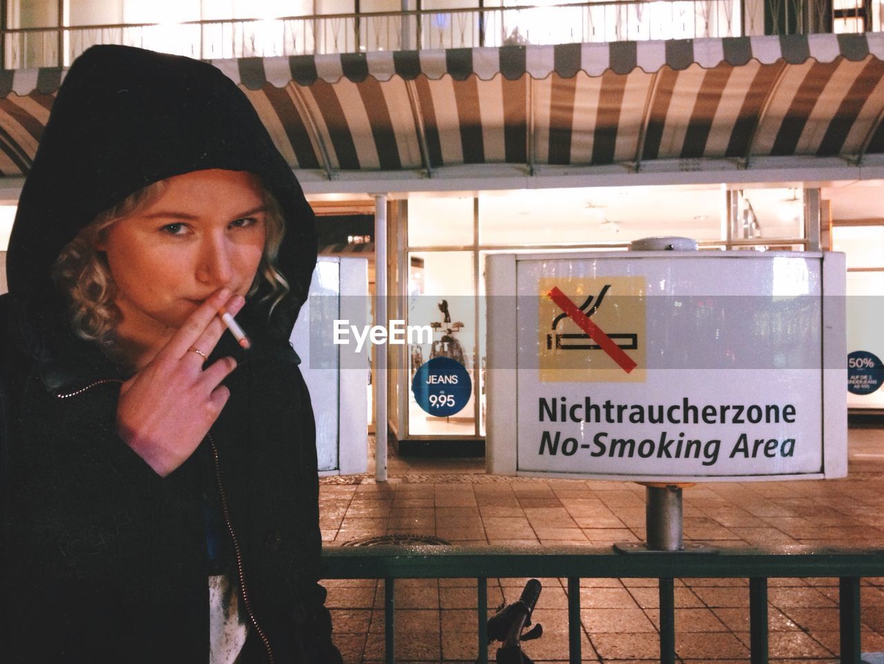 Young woman smoking in front of no smoking sign