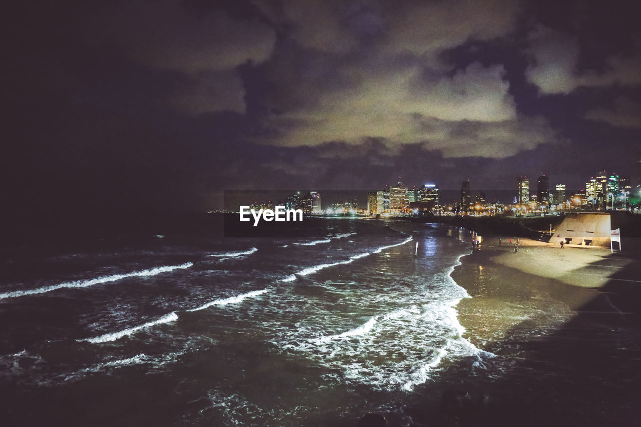 Aerial view of illuminated city by sea against sky at night