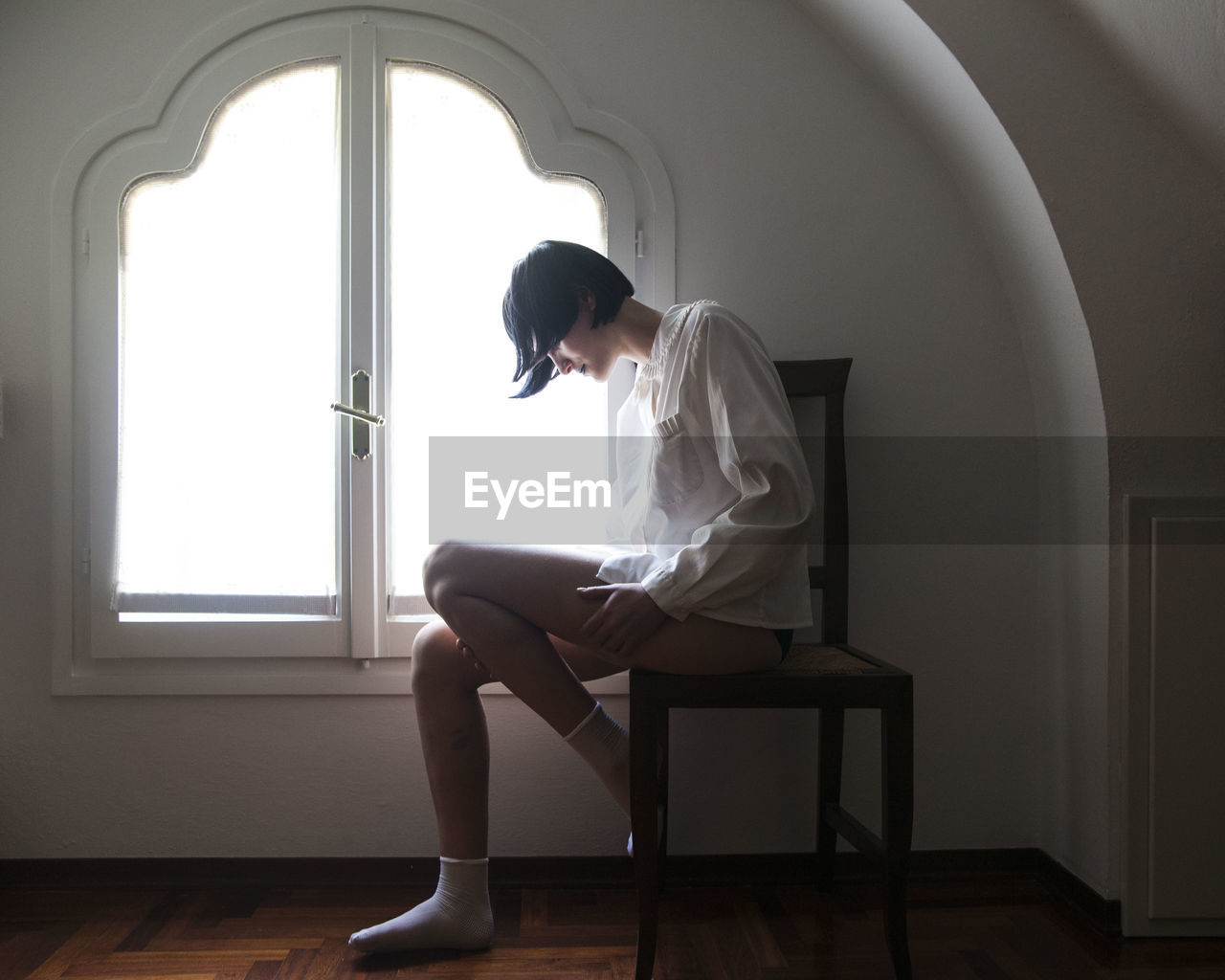 Full length of woman sitting on chair against window at home