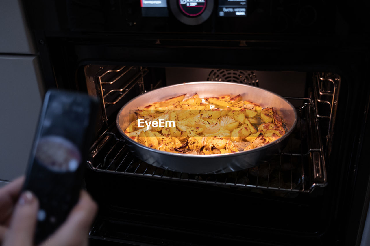 A food blogger takes pictures with phone and shoots food in the oven that she has cooked. 