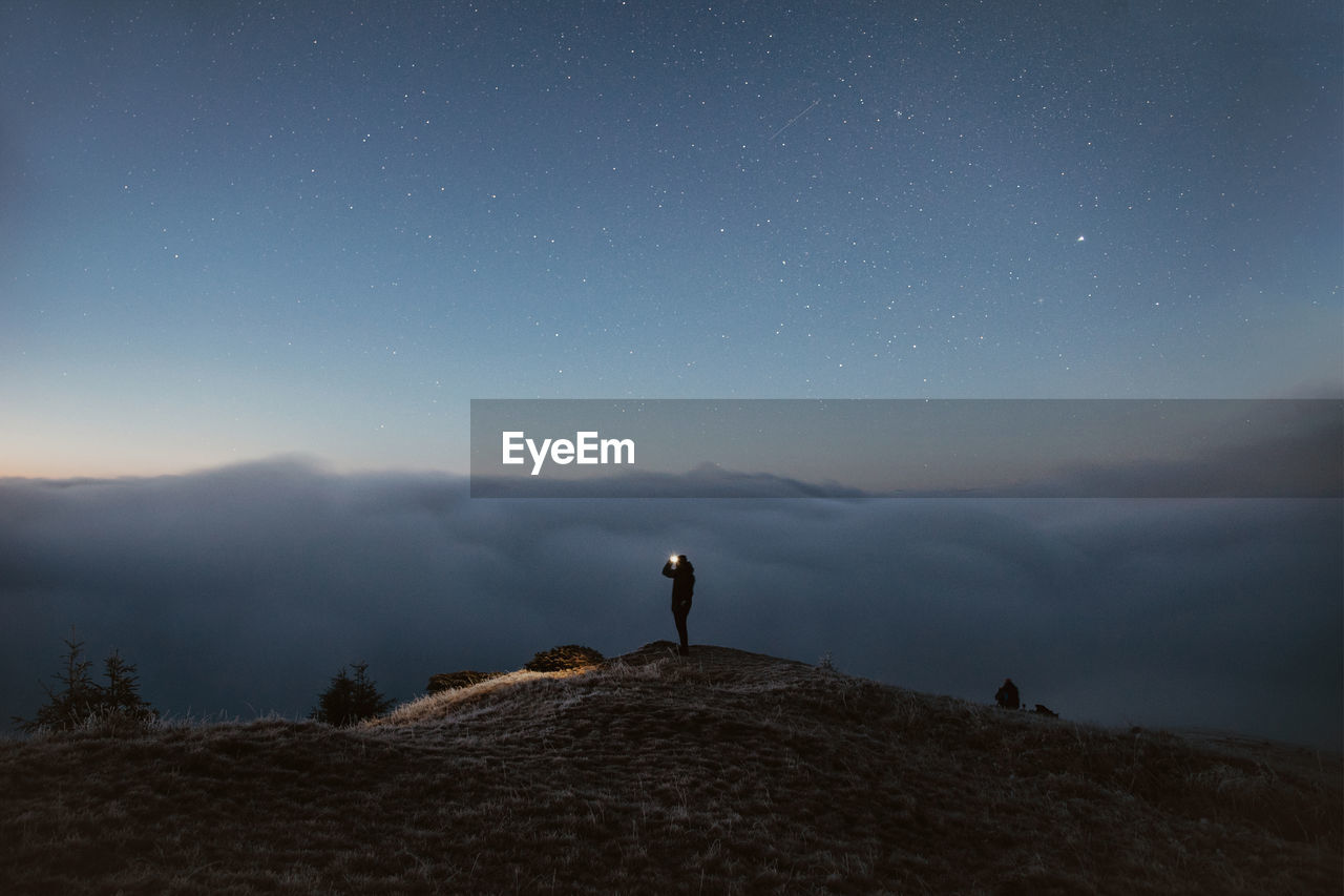 Person standing on the mountain above the clouds during the night
