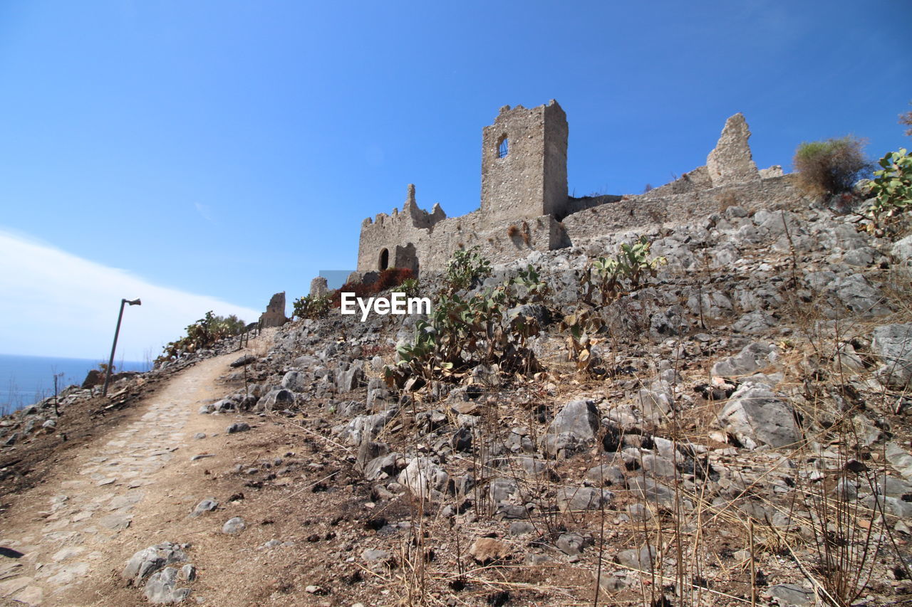 sky, architecture, history, the past, nature, built structure, travel destinations, rock, land, travel, ruins, blue, ancient, building exterior, building, cliff, no people, fort, mountain, tourism, day, castle, scenics - nature, outdoors, sea, clear sky, cloud, terrain, old ruin, wall, low angle view, landscape, plant, beauty in nature, environment, water, coast, geology, ancient history, old, non-urban scene, fortification