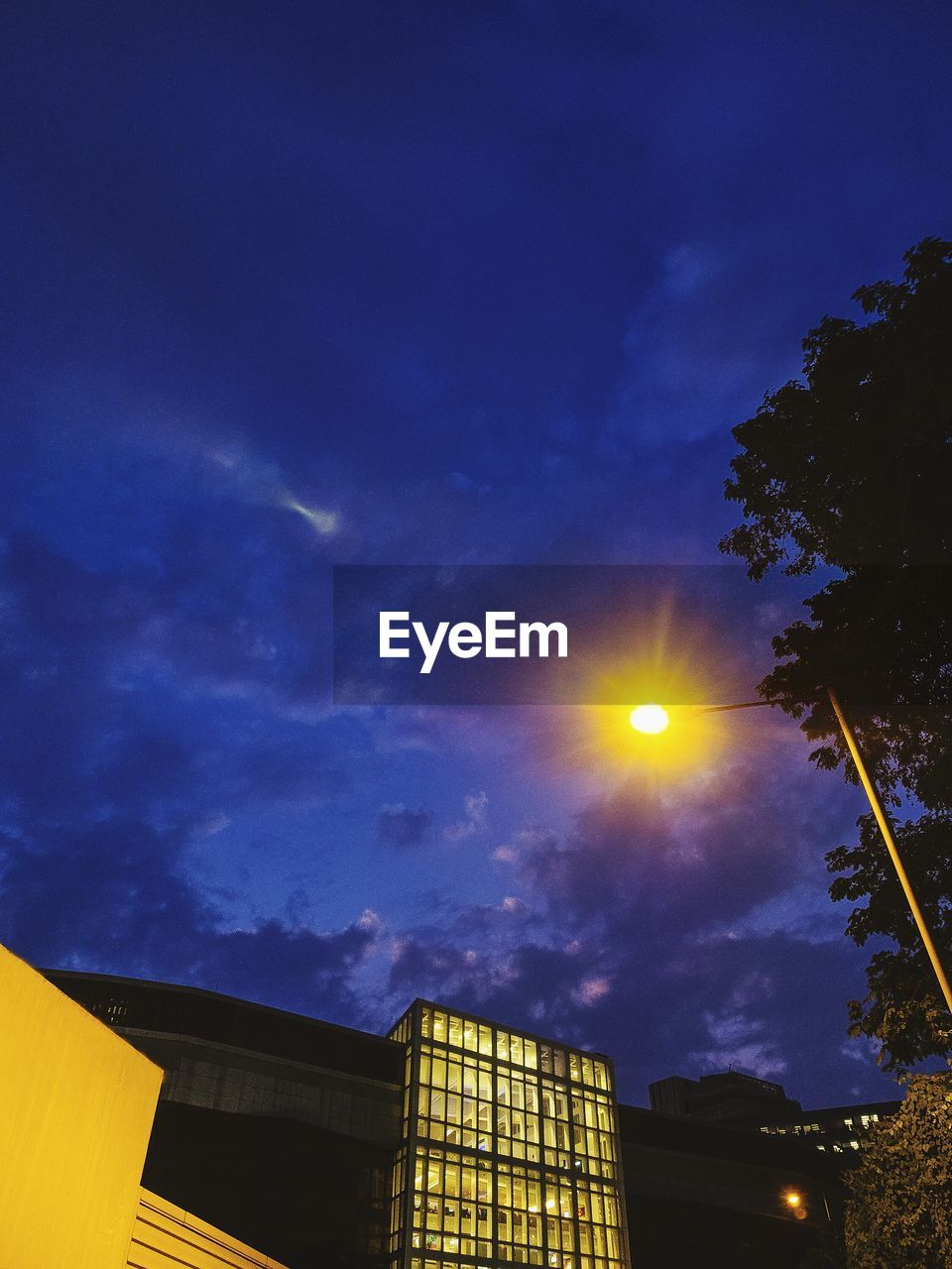 Low angle view of illuminated street light and buildings against sky