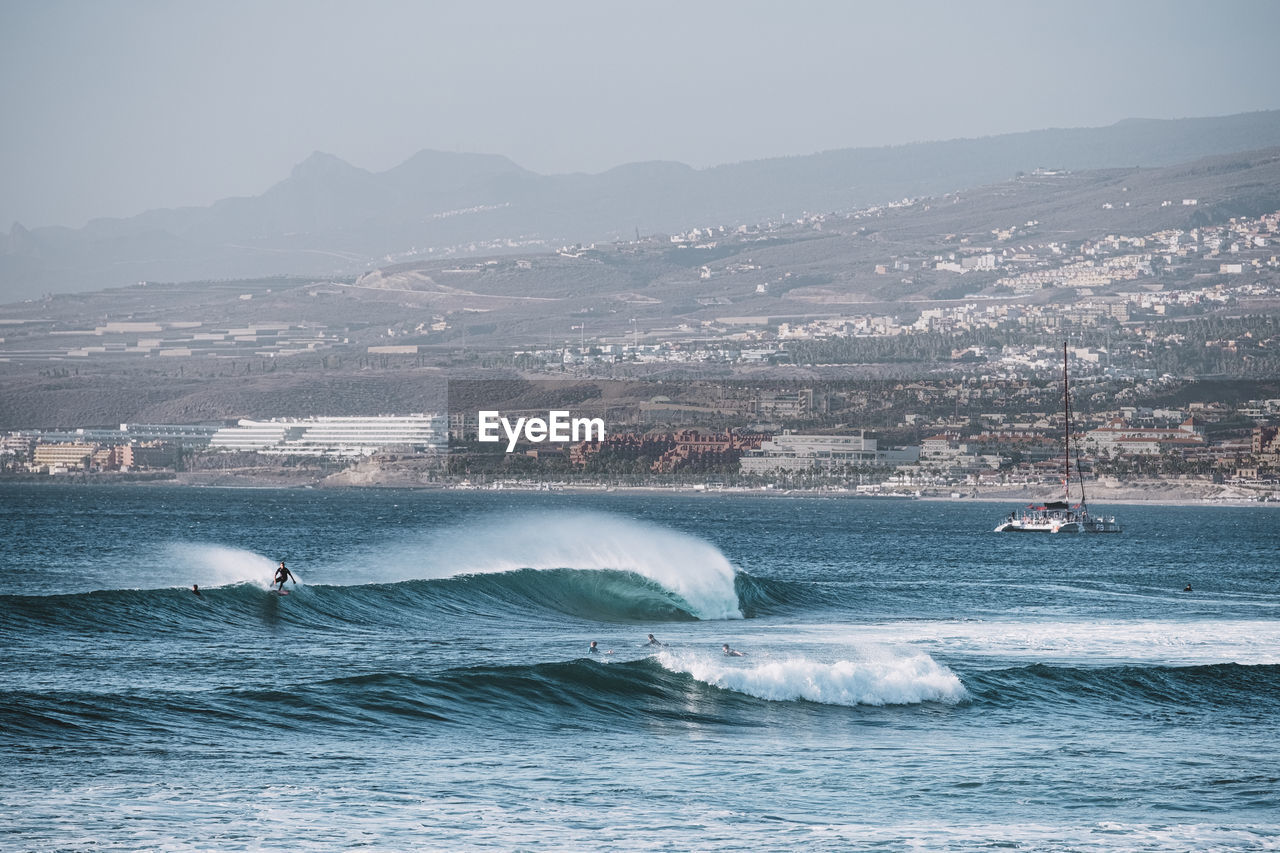 Pulled back view of breaking wave with city in background