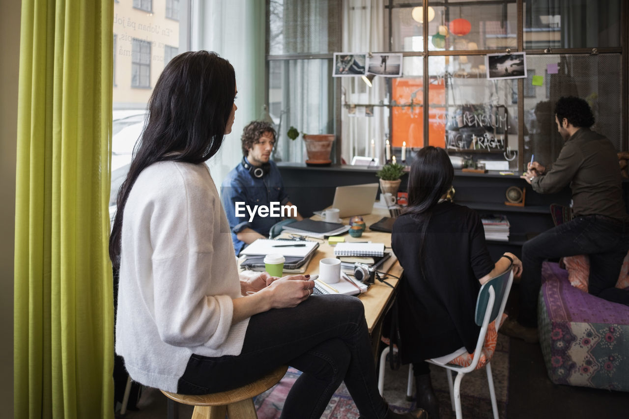 Creative team looking at man writing in adhesive note at modern office