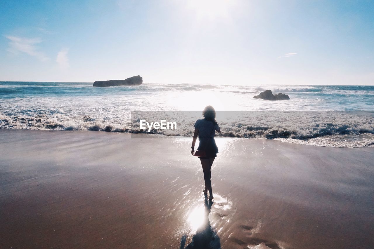 Rear view of young woman walking on shore against sky