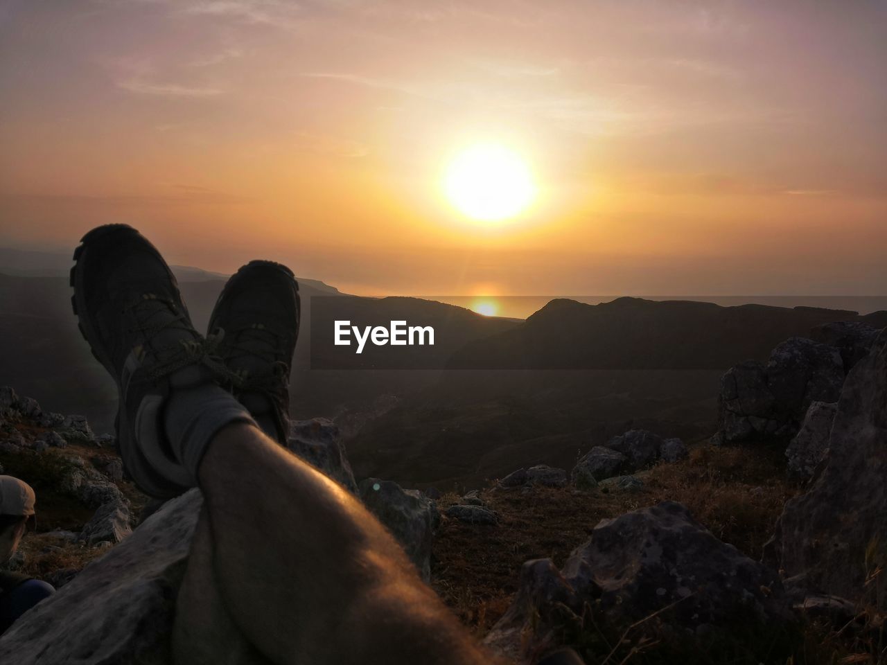 LOW SECTION OF MAN RELAXING ON ROCK DURING SUNSET