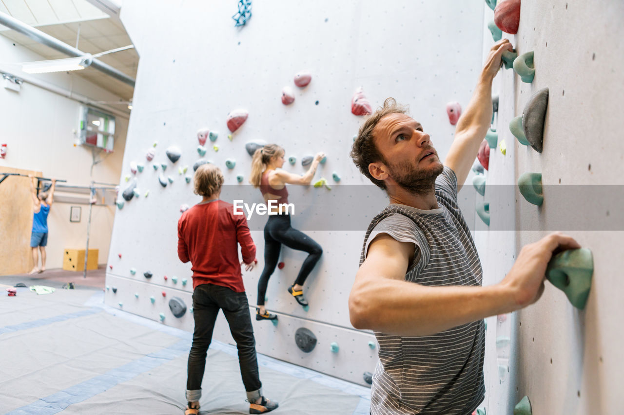 Male and female students practicing wall climbing while mature coach training in gym