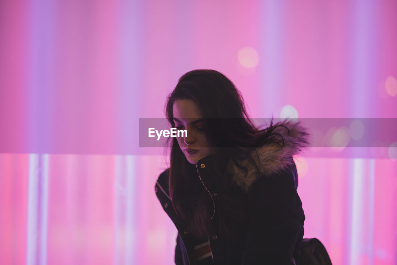 Thoughtful young woman standing against pink light at night