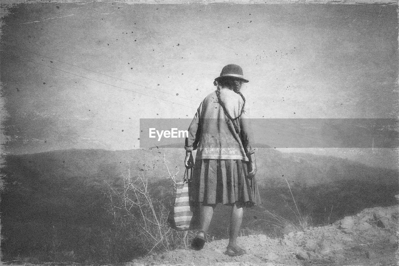 Full length rear view of woman with bag walking on field against sky