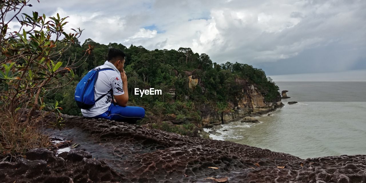 Man sitting on cliff against sea