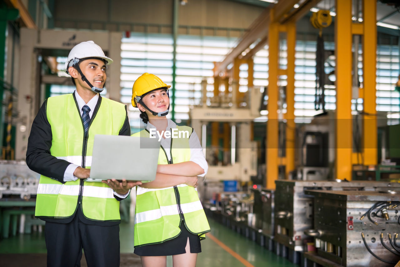 Engineers holding laptop looking away in factory