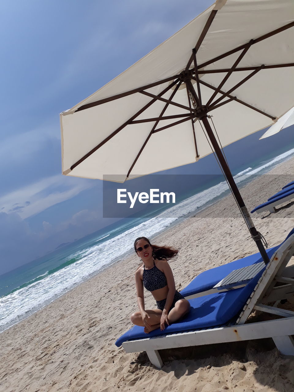 Tilt image of woman sitting on deck chair at beach