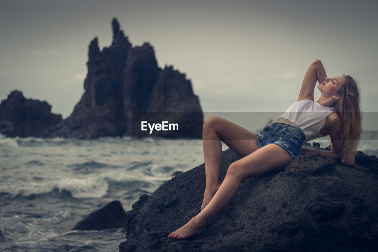 Woman lying on rock at beach against sky