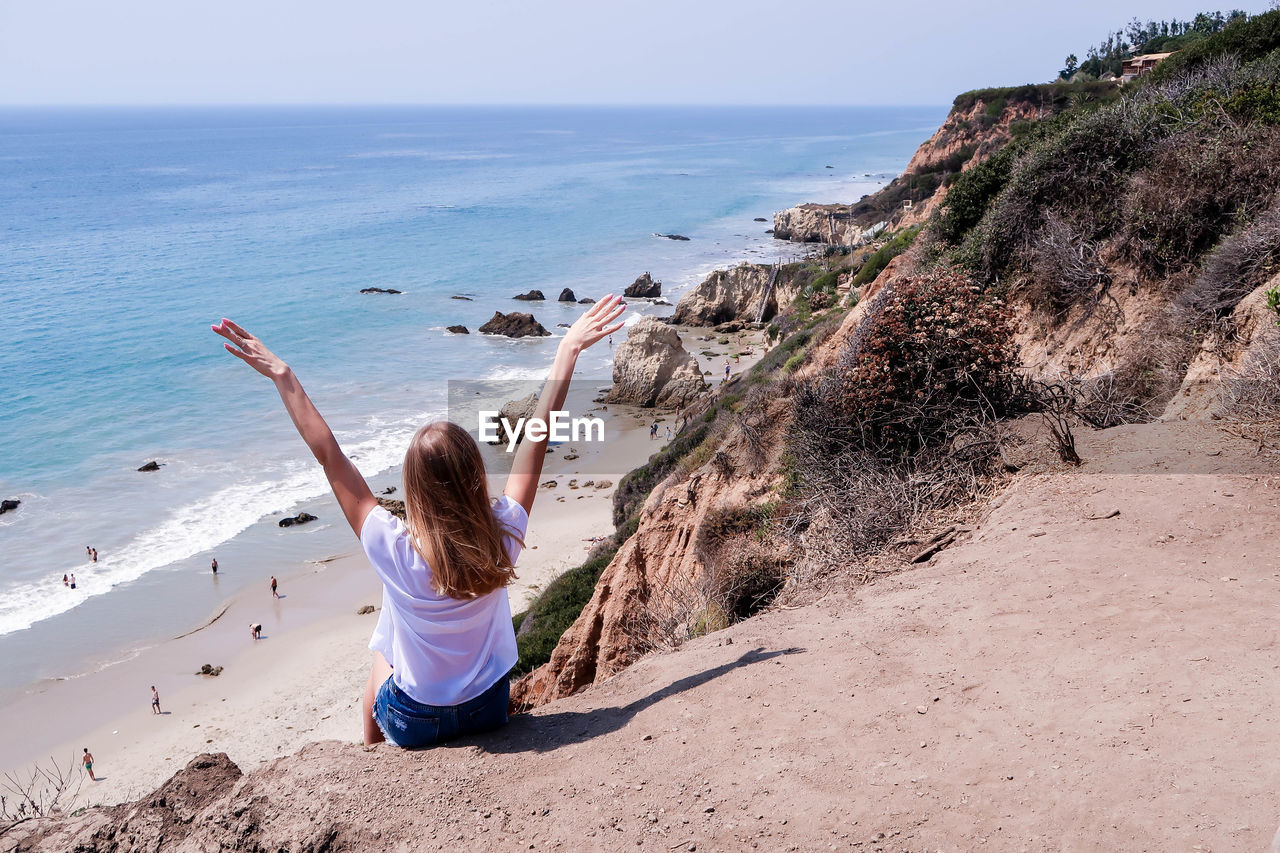 Rear view of woman sitting on cliff against sea