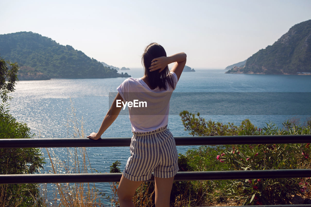 Woman in a white t-shirt and striped shorts and sunglasses stands on sea view  mountain in marmaris
