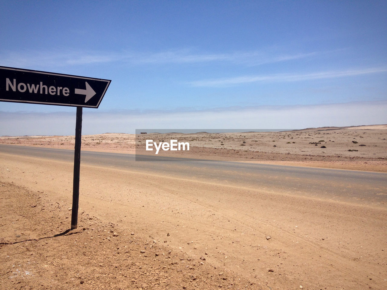 Road sign by highway at skeleton coast against sky