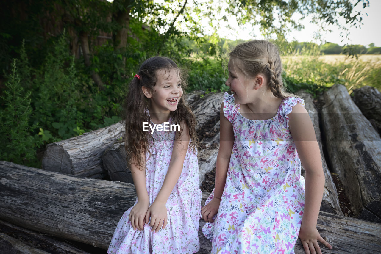 Smiling girls talking while sitting on log