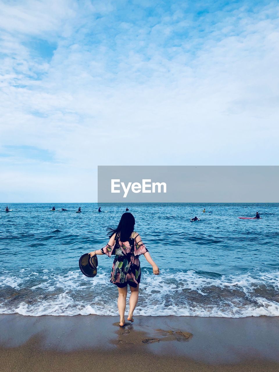 Rear view of woman standing at beach against sky