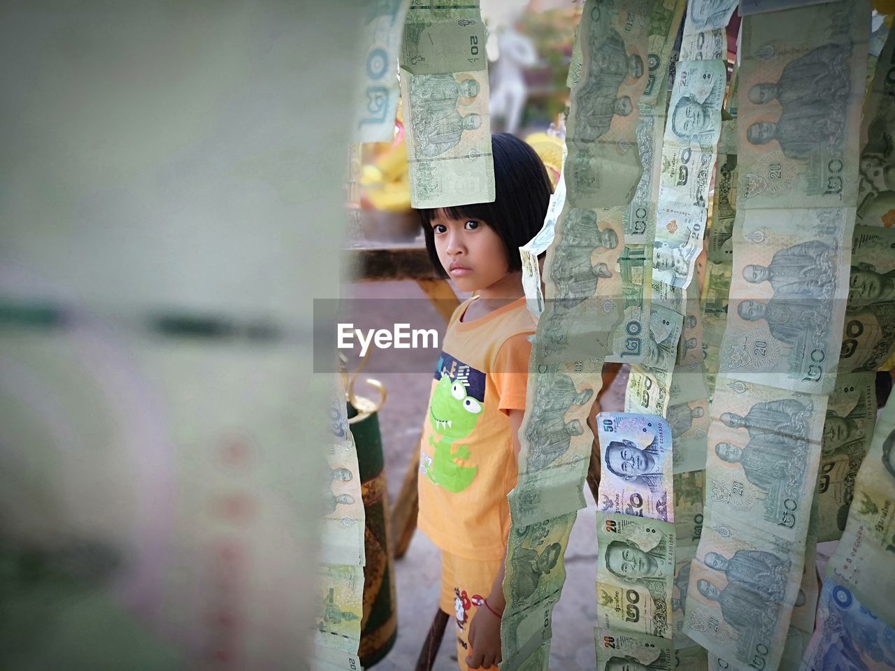 Side view of cute girl looking at paper currency hanging while standing outdoors