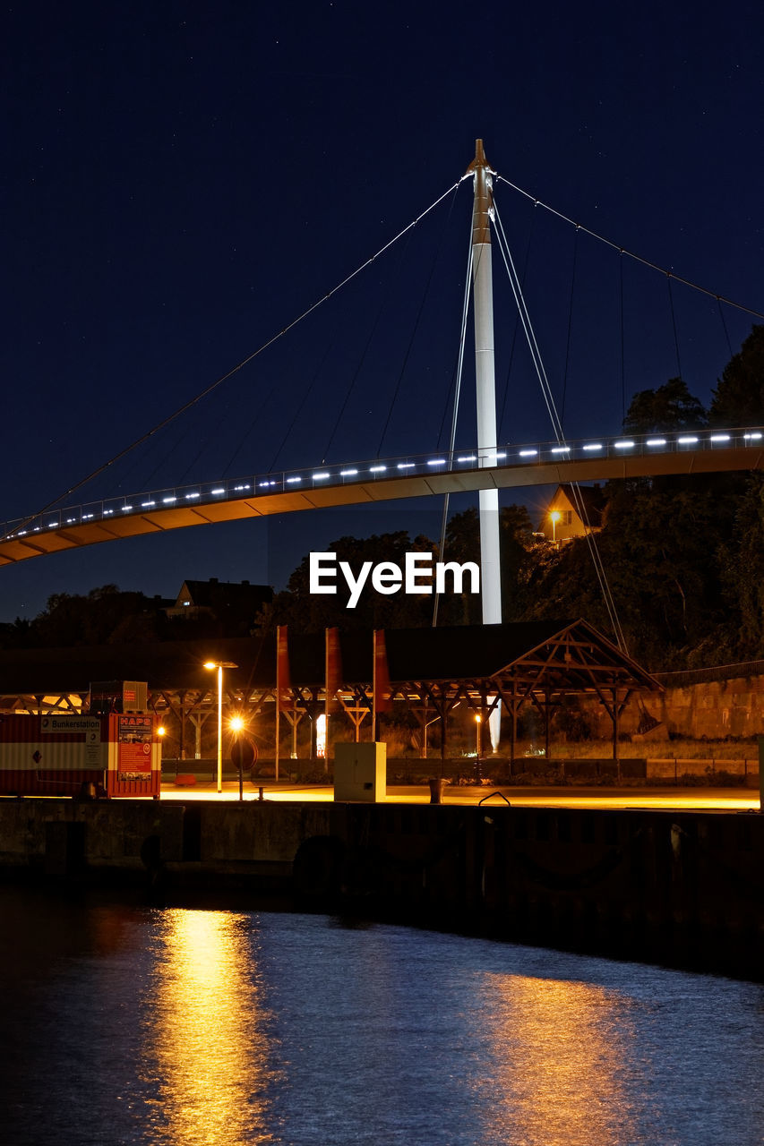 ILLUMINATED SUSPENSION BRIDGE OVER RIVER AT NIGHT