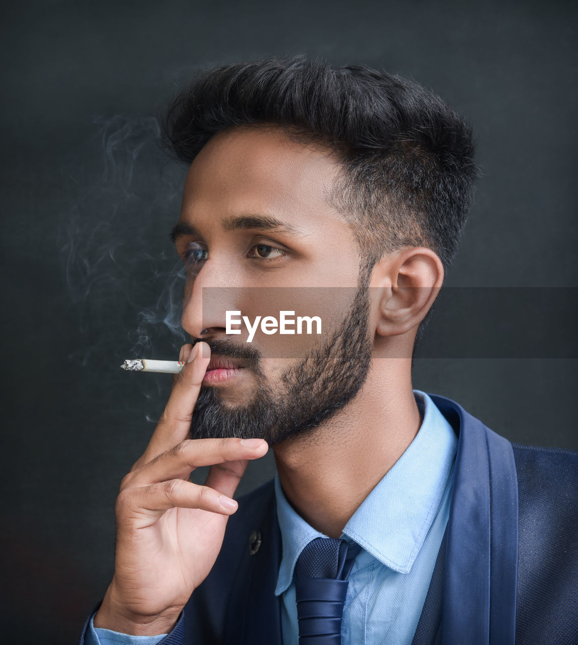 Young man smoking cigarette against black background