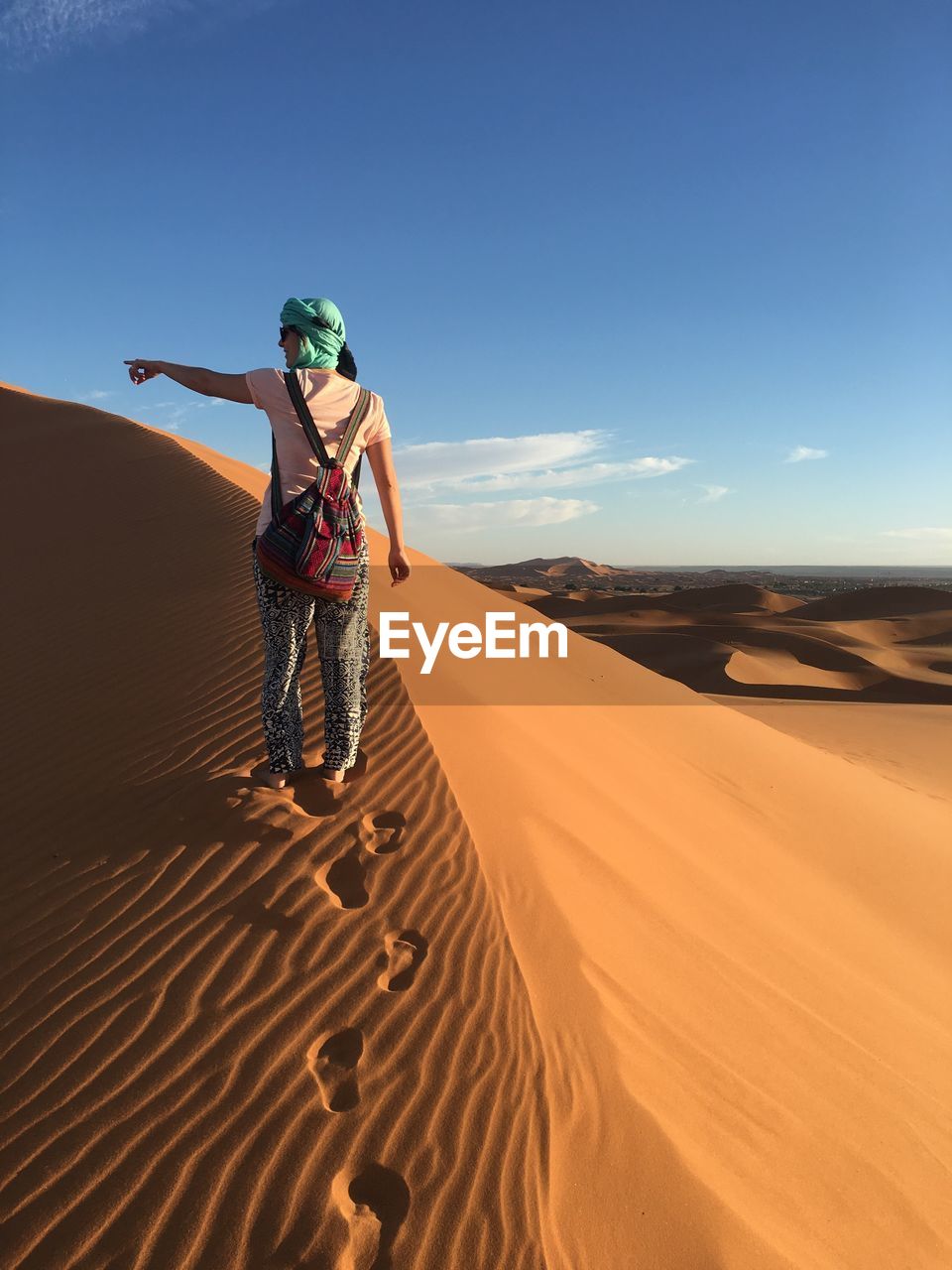 Rear view of woman walking on sand dune in desert against sky