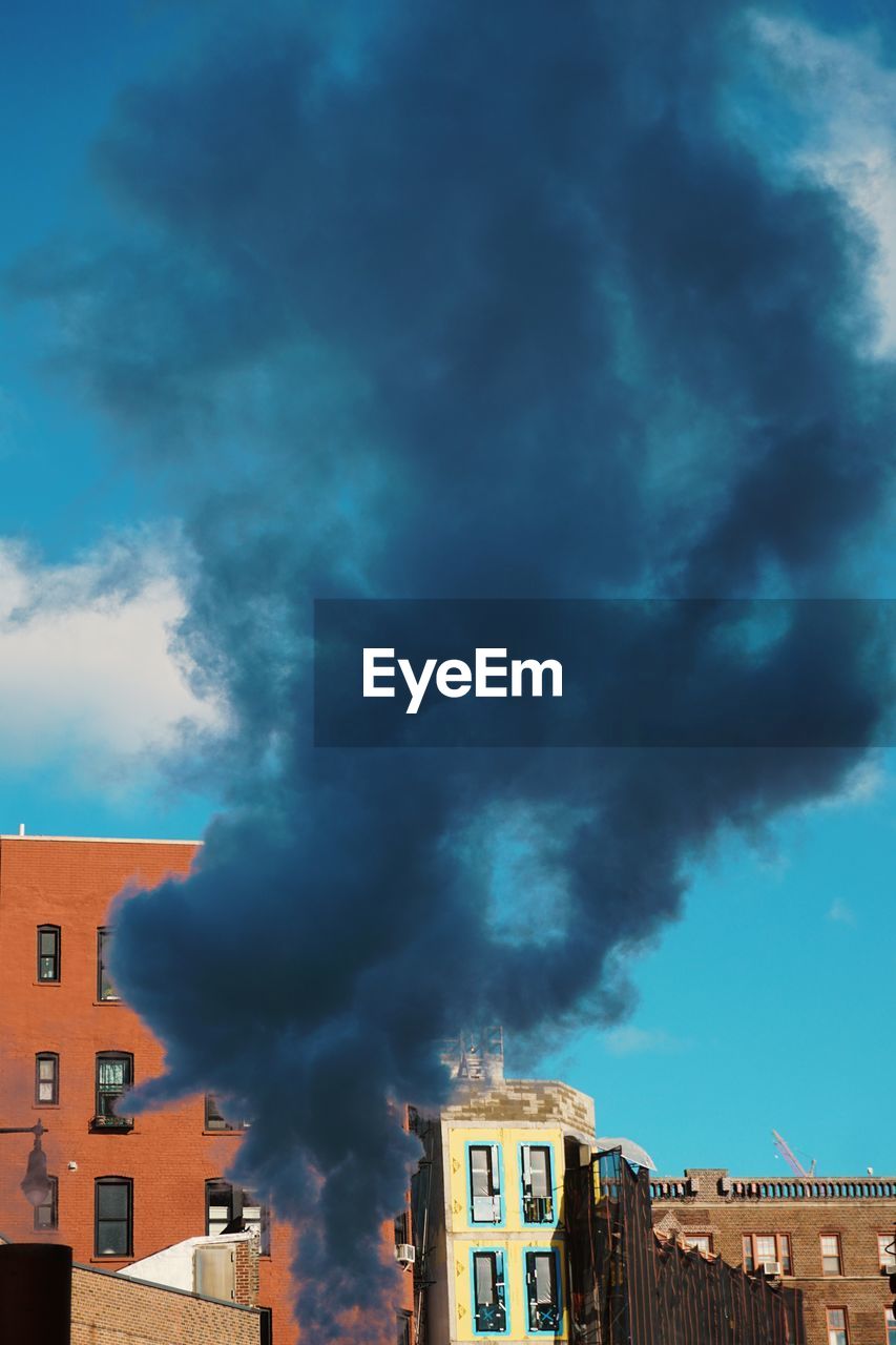 Low angle view of smoke emitting from chimney against blue sky