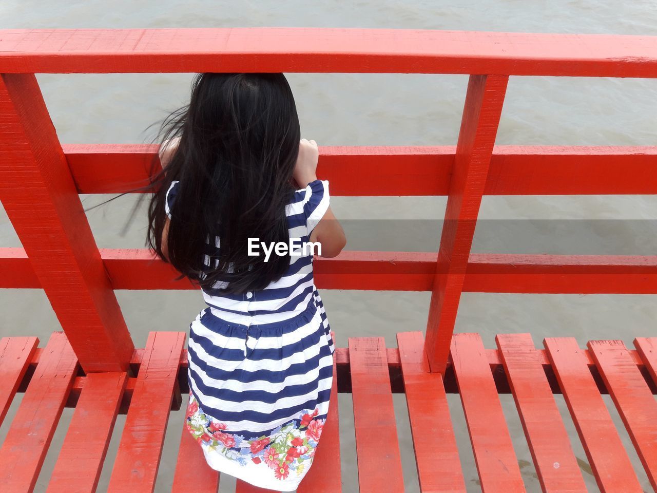 High angle view of girl standing on red footbridge over river