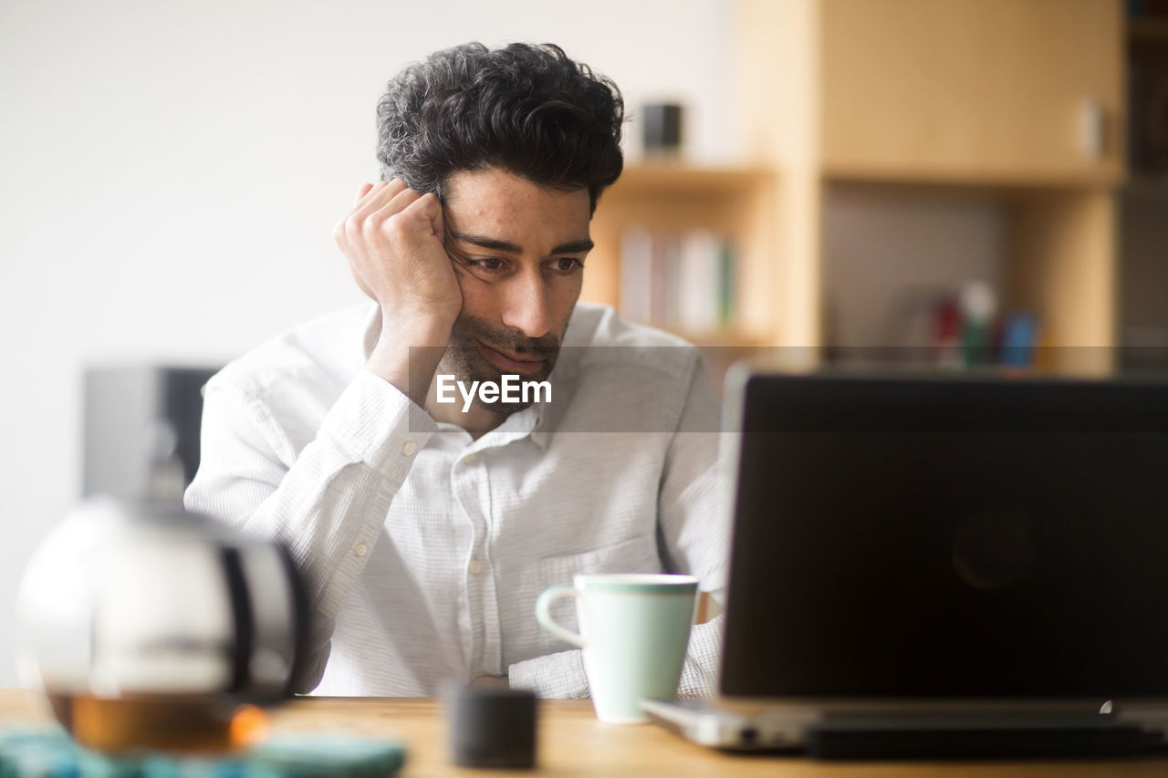 Portrait of businessman at desk looking at laptop