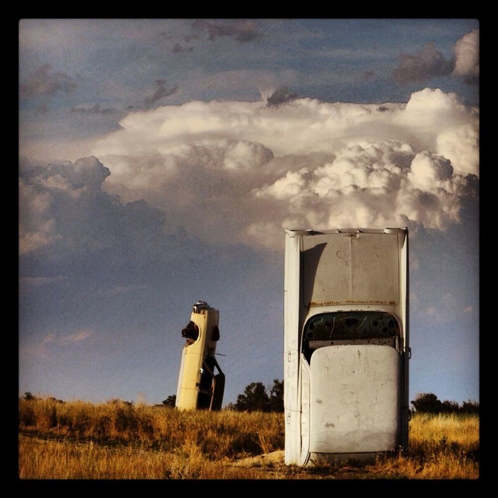 Abandoned car on grassy field against cloudy sky