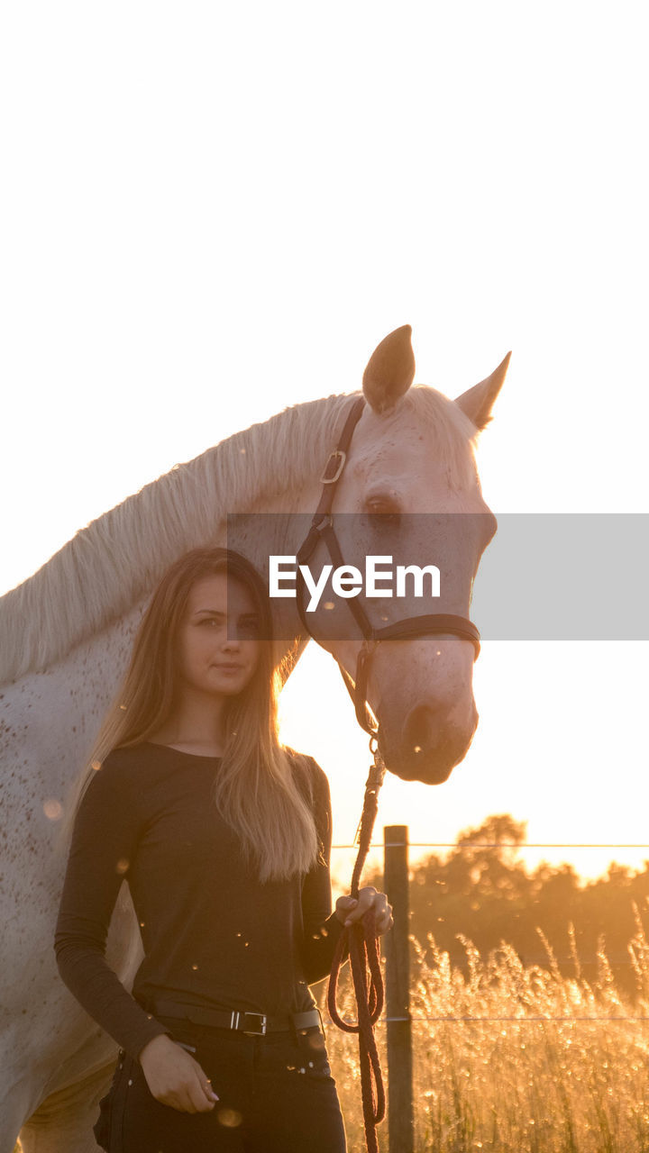 Portrait of young woman standing with horse on field against sky