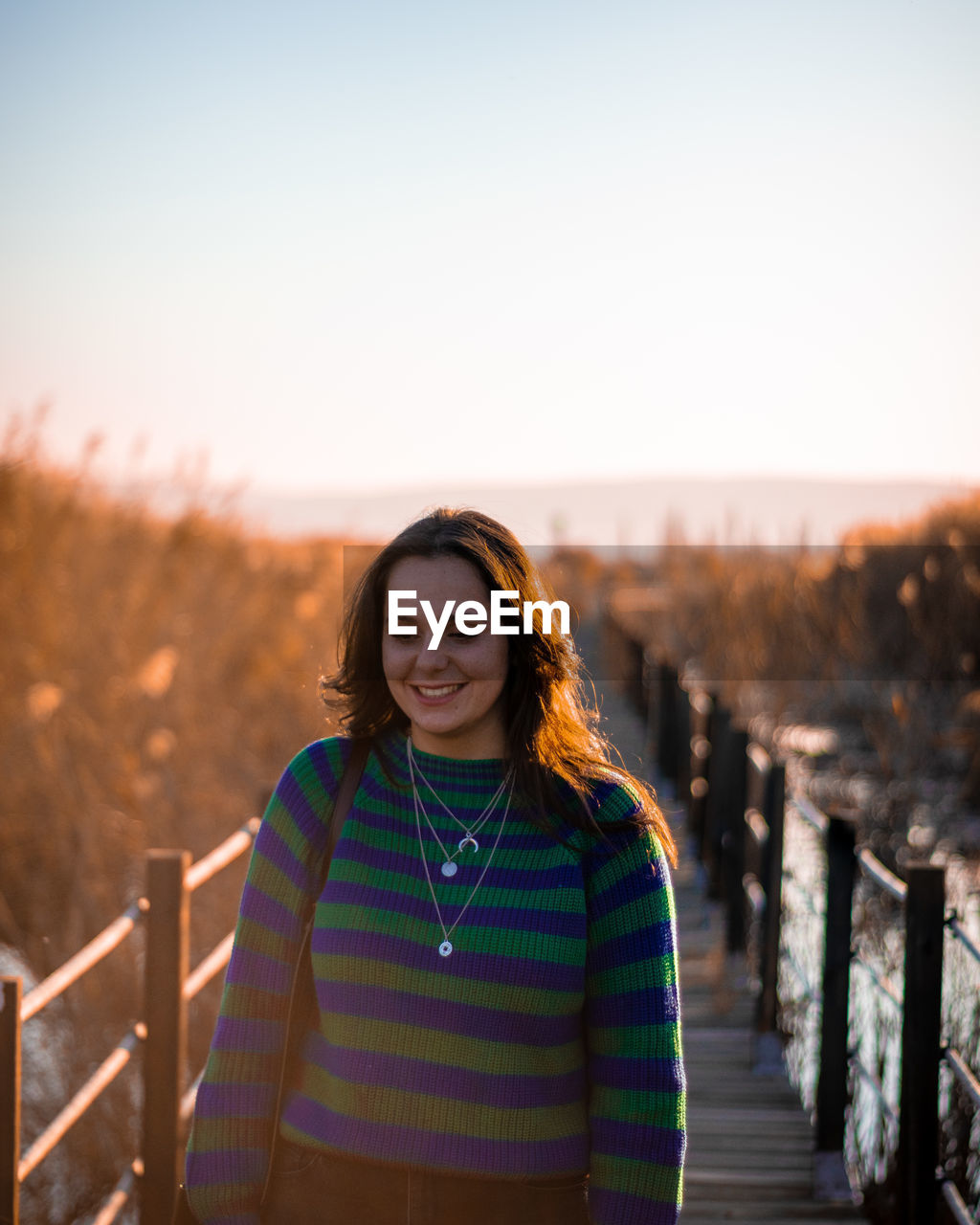 PORTRAIT OF SMILING WOMAN STANDING AGAINST SKY DURING SUNSET