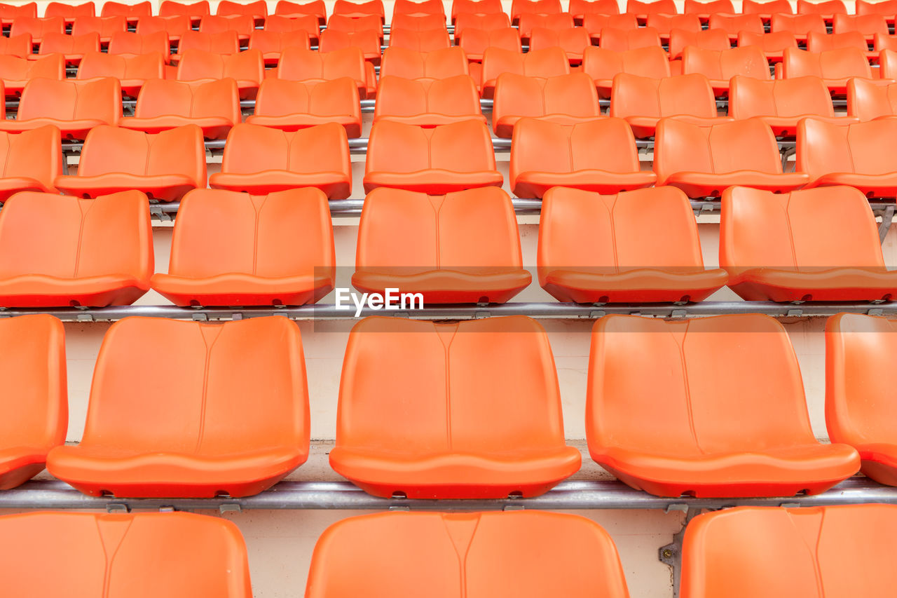 Rows of empty orange plastic grandstand seats at an indoor sport stadium. 