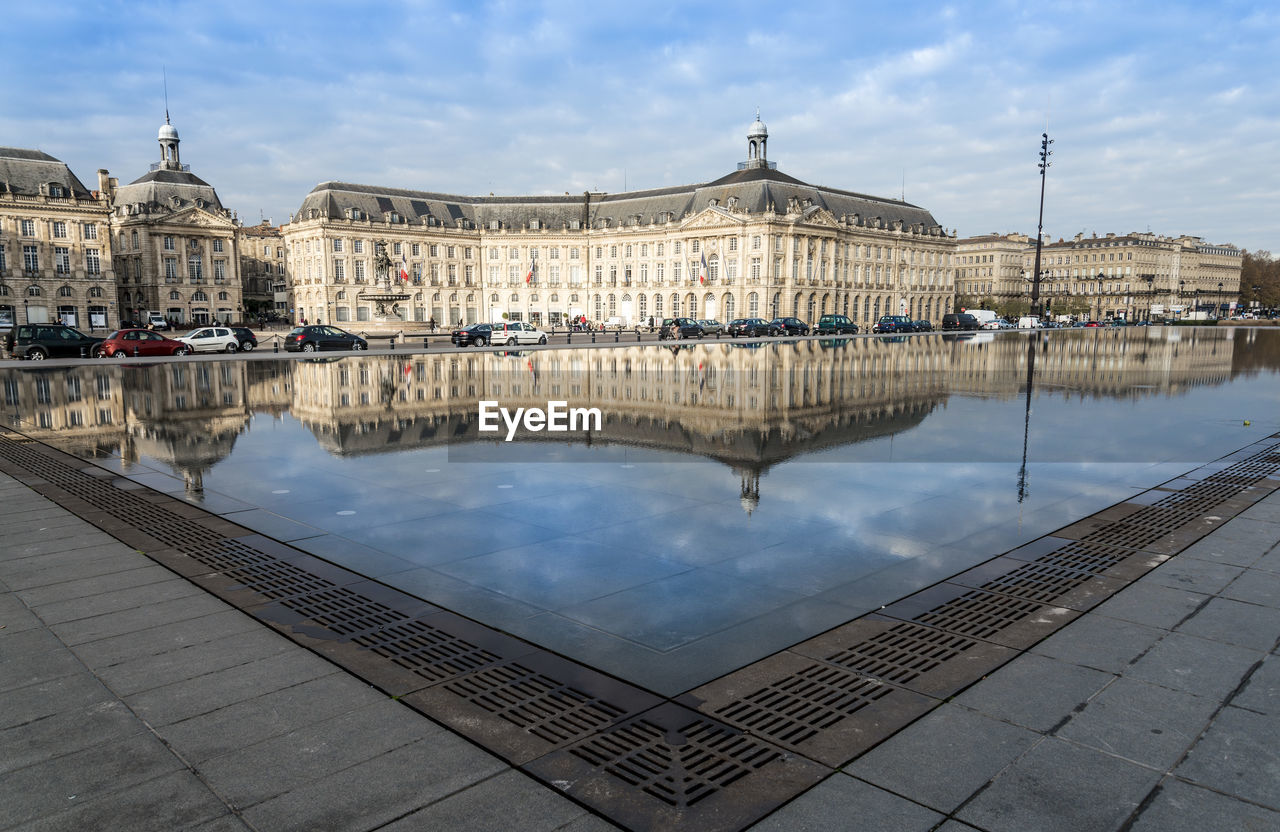 Reflection of old building in lake water against cloudy sky