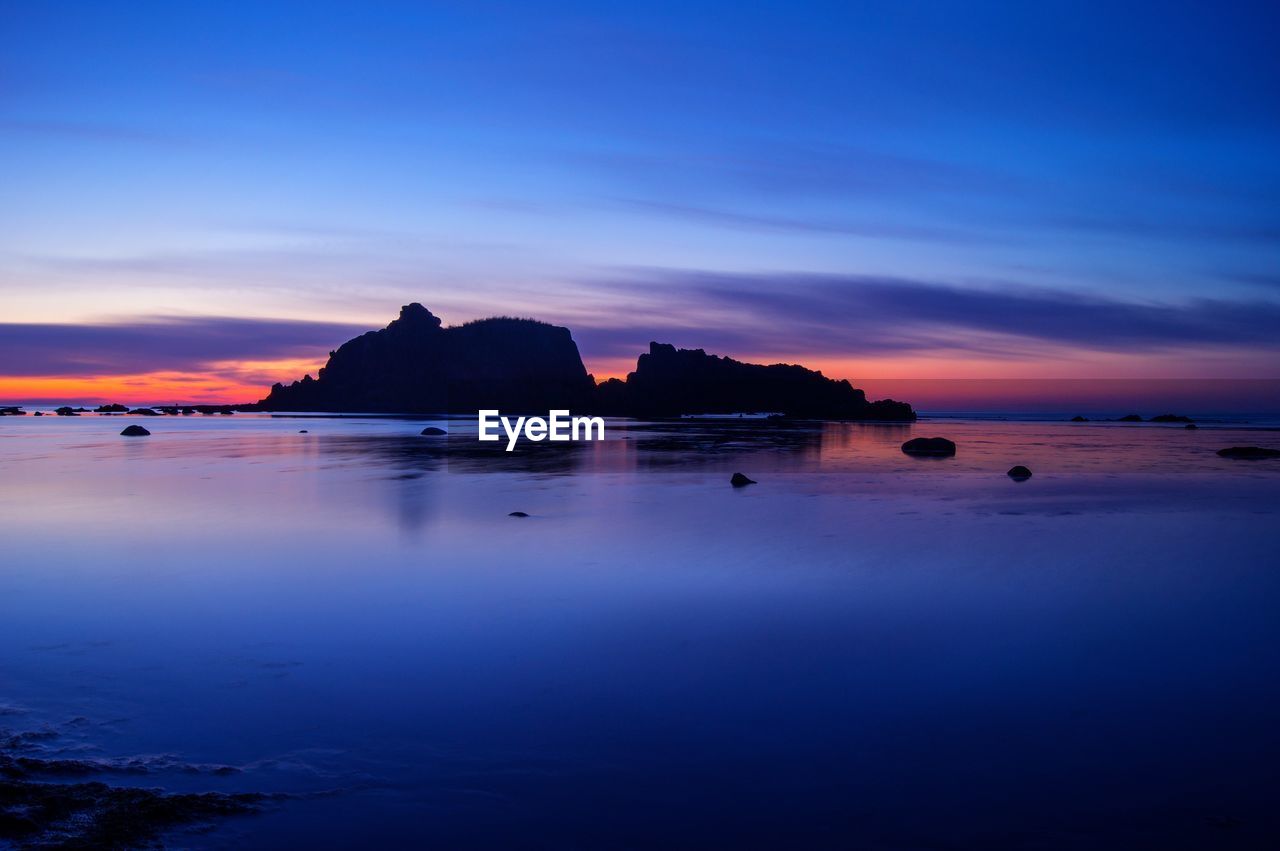 Silhouette headlands in calm sea against the sky