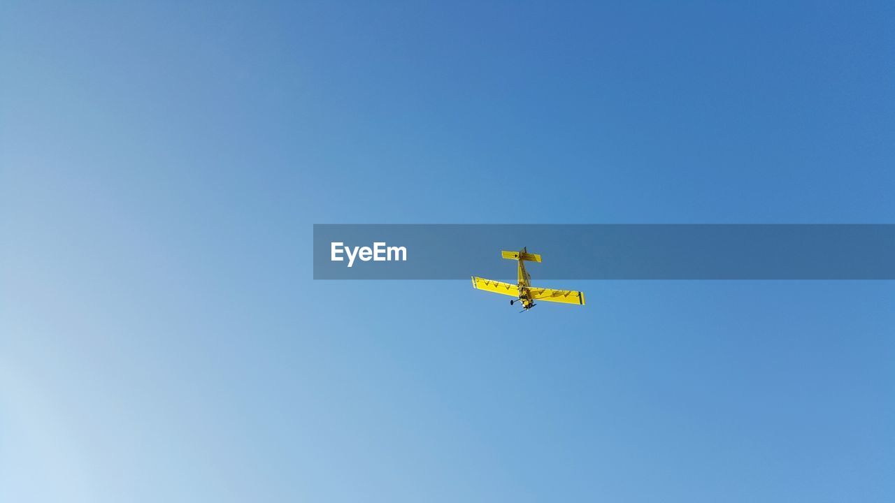 Low angle view of yellow airplane flying against clear blue sky