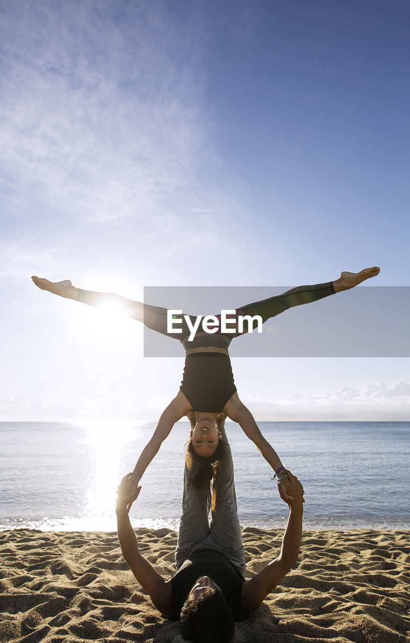 Determined multi-ethnic couple doing yoga on shore against sky
