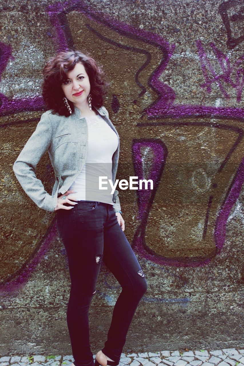 Portrait of fashionable young woman standing by graffiti wall