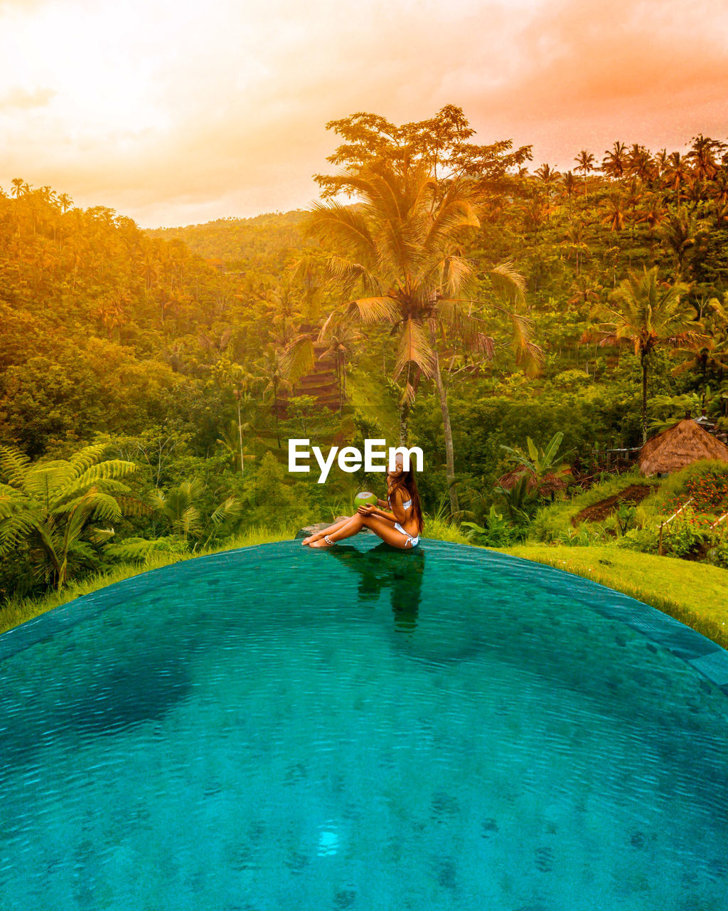 A girl sitting on the edge of a pool in the middle on jungle in bali, indonesia