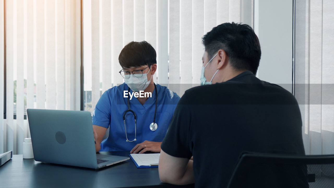 Patient and doctor wearing mask having discussion at clinic