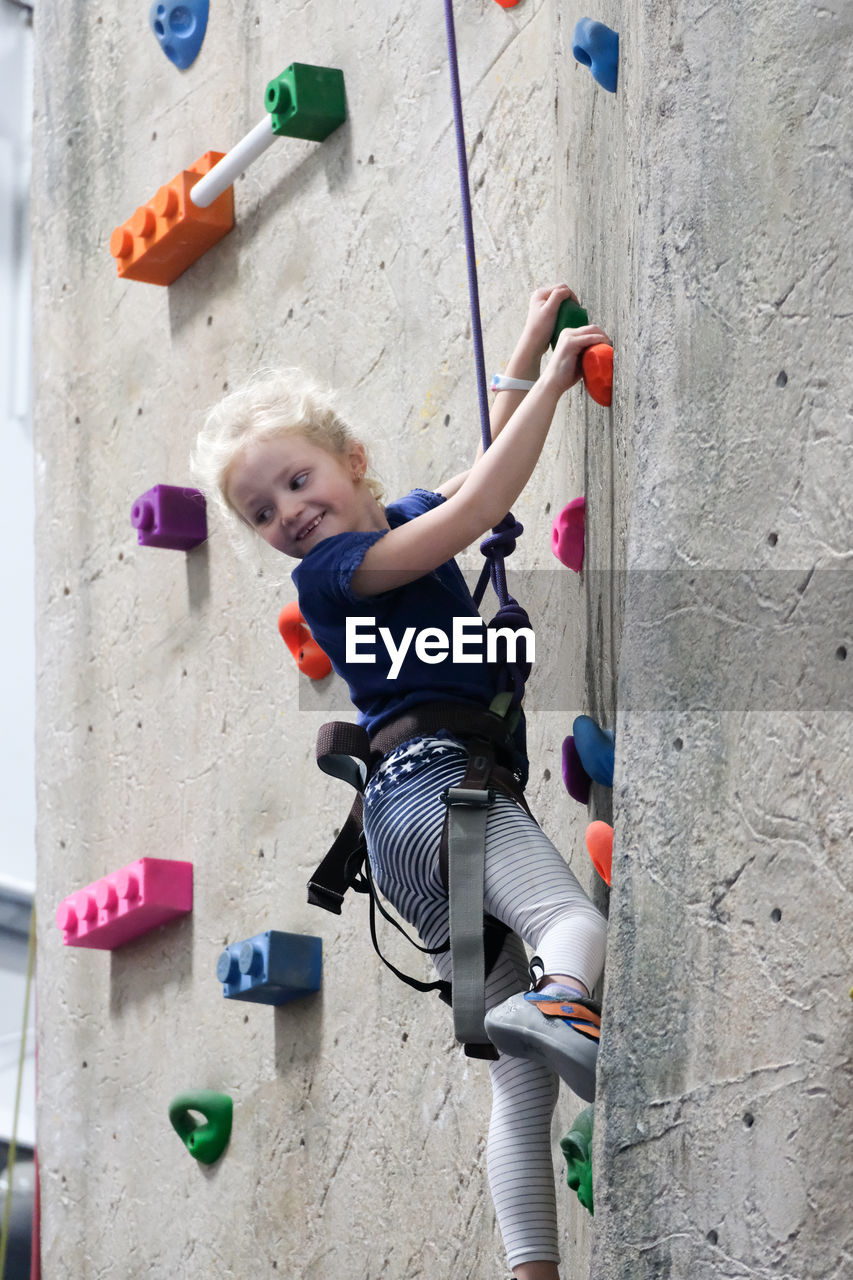 Young girl climbing rock wall at indoor rock climbing gym