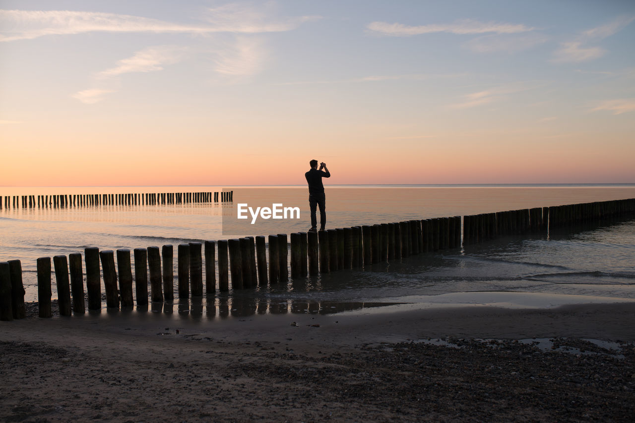 Rear view of man standing at beach during sunset