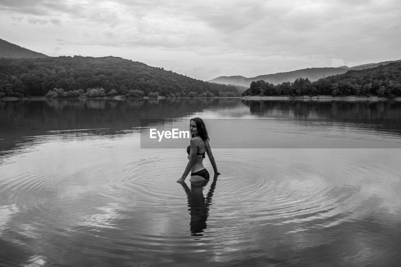 Woman standing in lake against sky